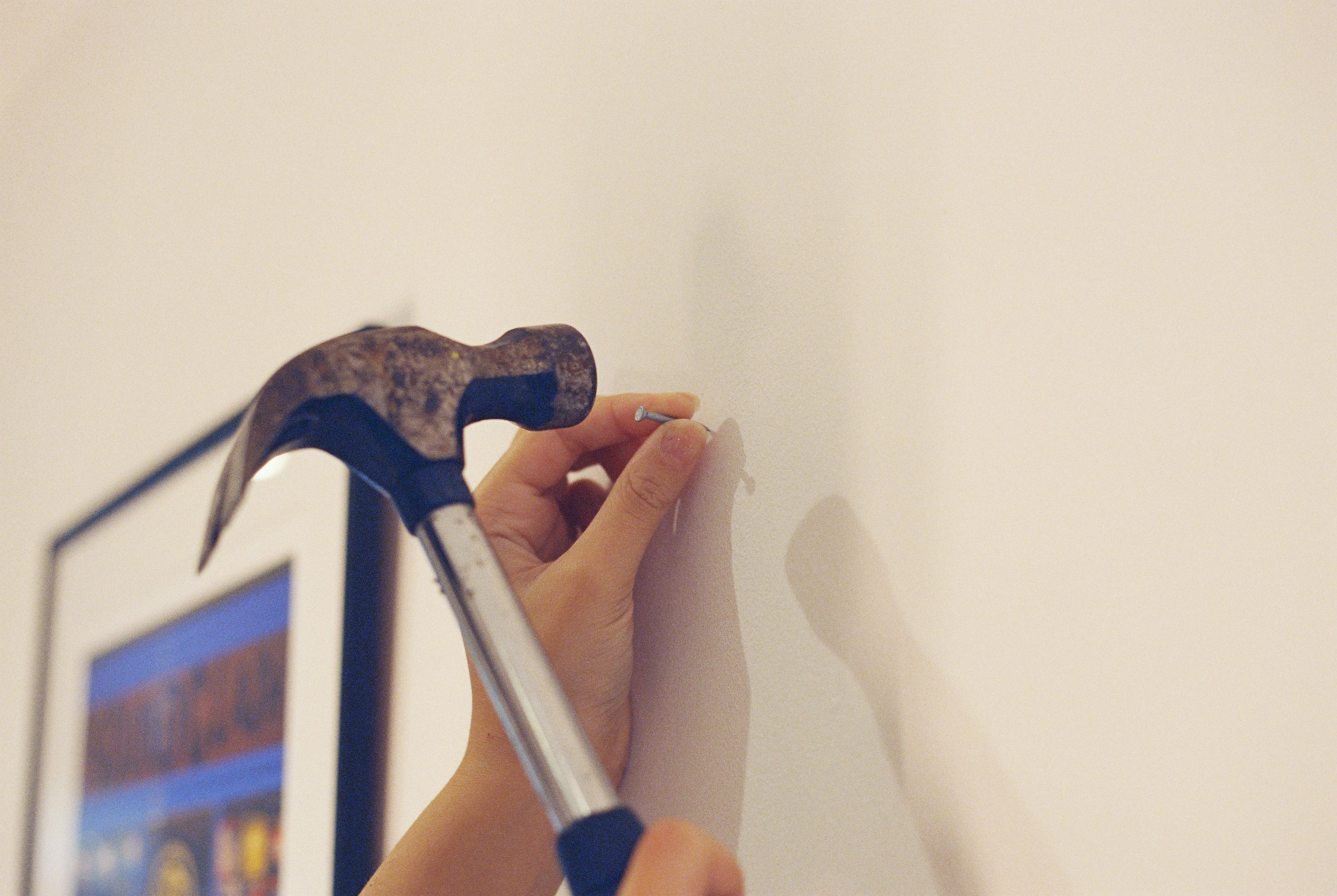 Hands hammering a nail into a wall to hang a picture